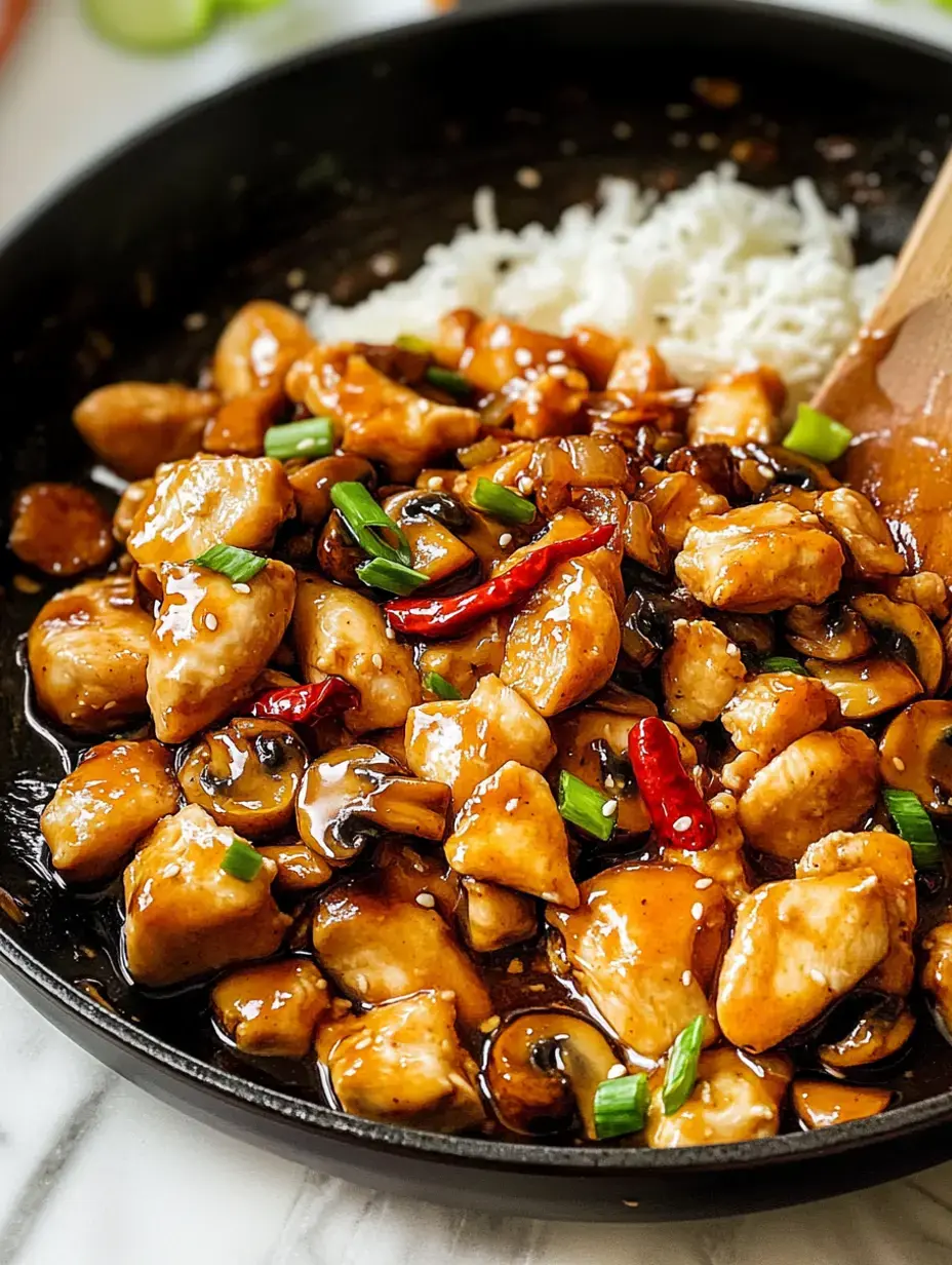 Sautéed chicken with mushrooms and green onions swimming in glossy sauce, sitting next to steamy white rice in a skillet.