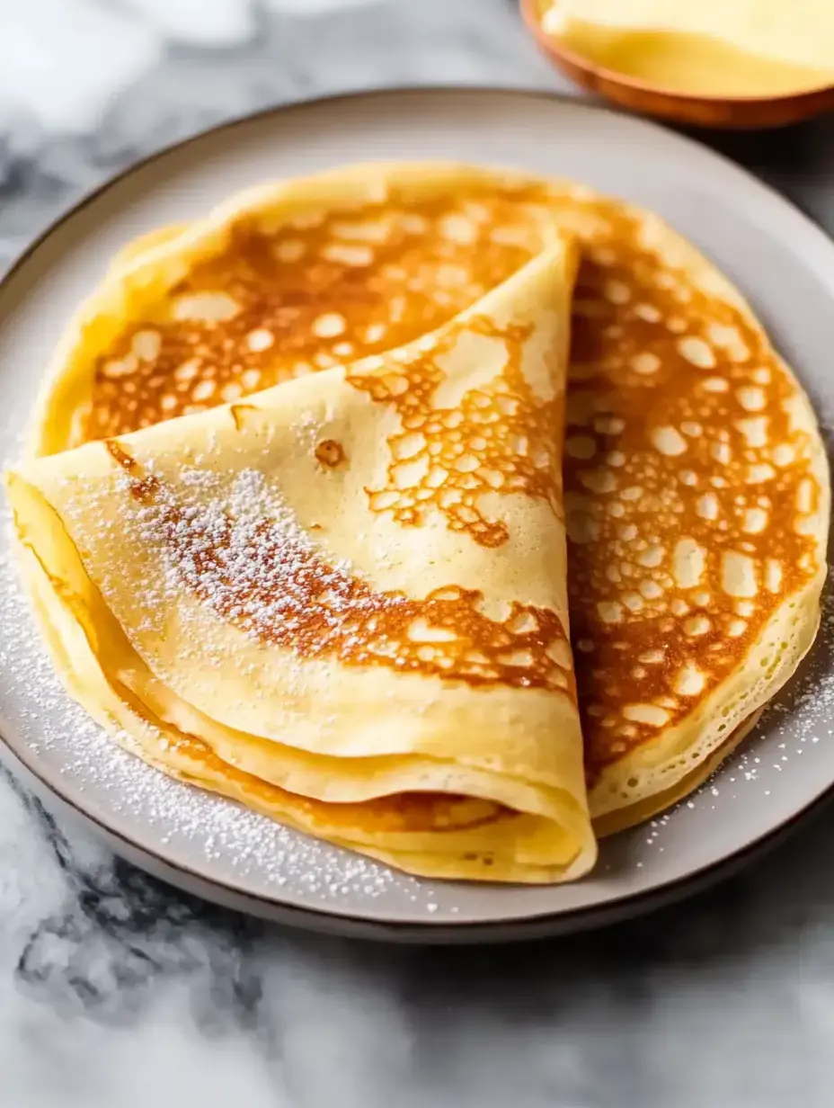 A plate full of warm, brown crepes topped with powdered sugar.