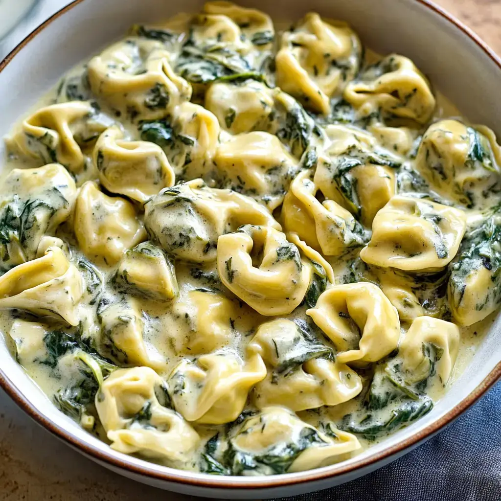Bowl of tortellini with spinach and creamy cheese sauce.