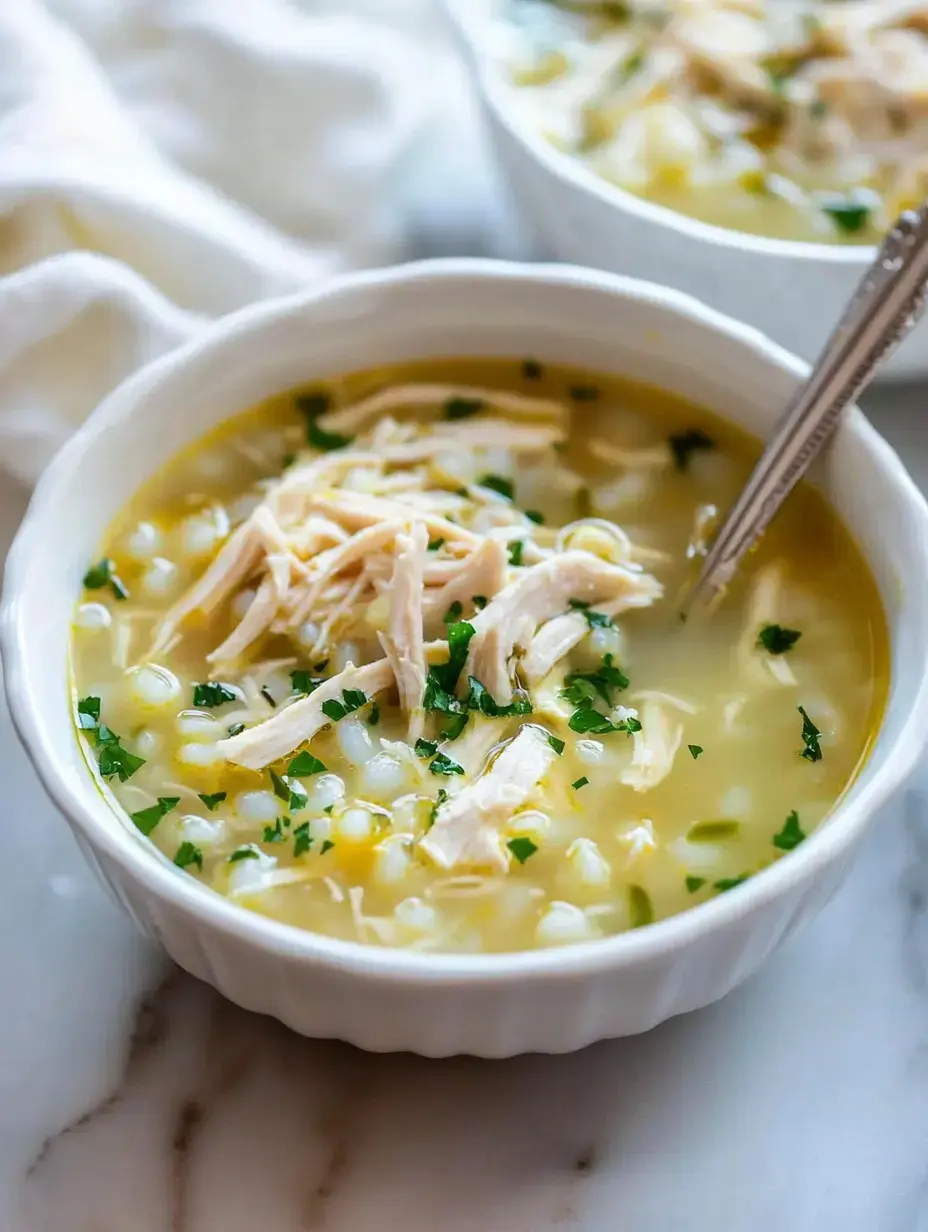 A bowl of chicken soup with shredded chicken, corn, and sprinkled parsley on top.