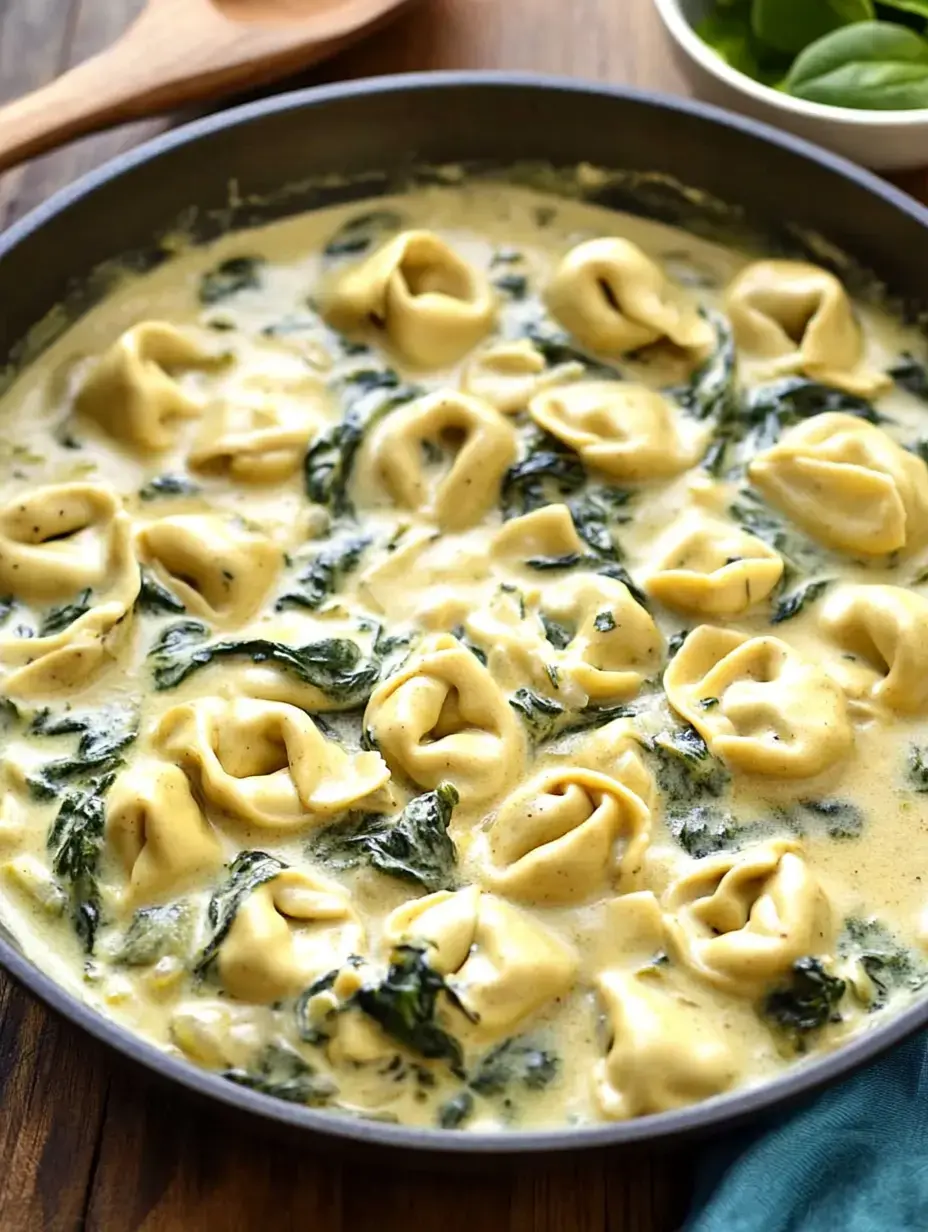 Tortellini and spinach coated in creamy sauce, bubbling in a skillet.